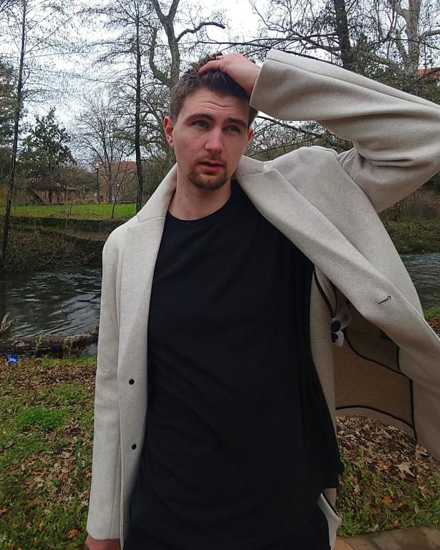 Conor in a cream coat beside a river