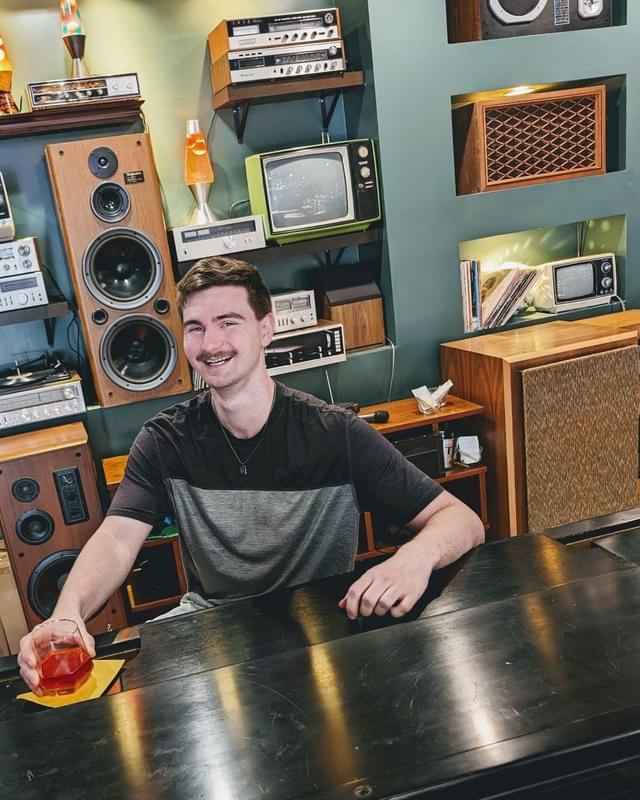 Conor smiling at a table in front of a wall of vintage audio equipment